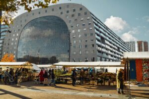 Bustling street market in front of Rotterdam's Markthal, showcasing modern architecture and local life.